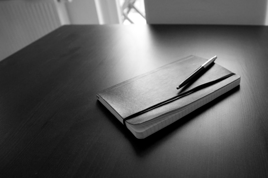 Closed notebook with a pen on top laying on top of a desk